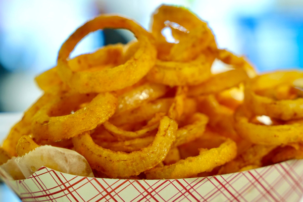 A close-up, eye-level shot of a basket overflowing with golden-brown, crispy fried onion rings.